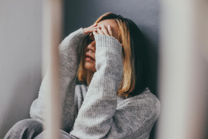 Person in a gray sweater sitting, looking distressed, with hands covering their face, illustrating a terrible Christmas experience.