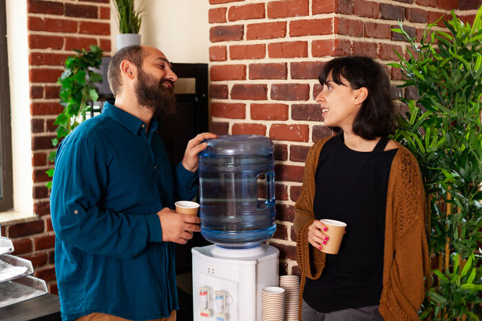 Two colleagues chatting by an office water cooler, illustrating casual workplace interactions and HR dynamics.