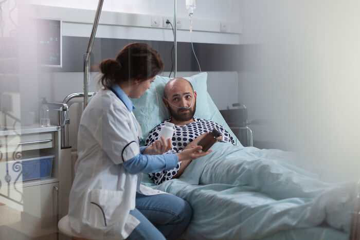 Person in hospital bed during Christmas, listening to a nurse, symbolizing a challenging holiday experience.