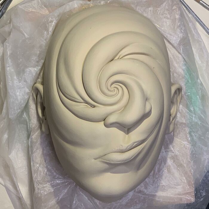 Surreal sculpture featuring a face with a swirling spiral design, blending realism and surrealism.