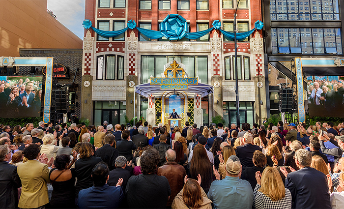 Crowd gathered outside the Scientology building, with blue decorations, during a public event.