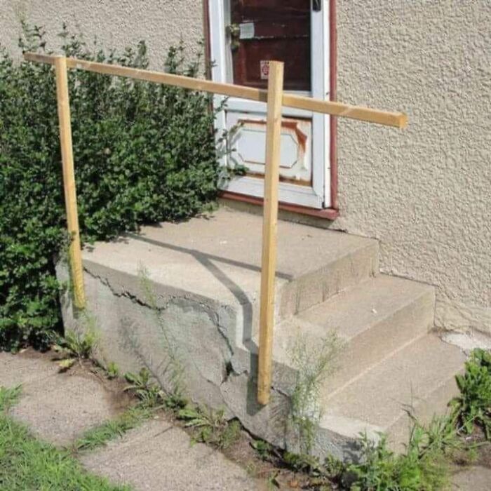 Cheap construction fail featuring a makeshift wooden handrail on cracked concrete steps.