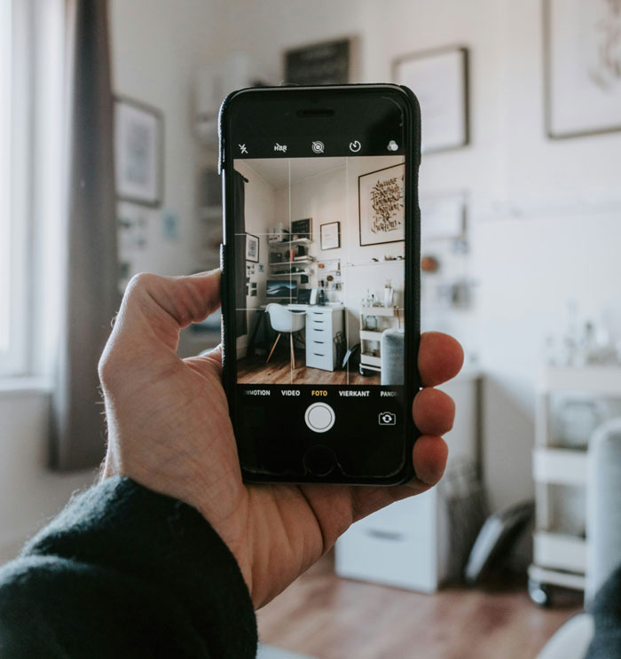 Hand holding a smartphone taking a photo of a home office, highlighting security measures in a digital setting.