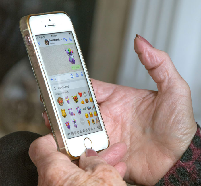 Person holding a smartphone, browsing emojis on a messaging app, highlighting security measures awareness.