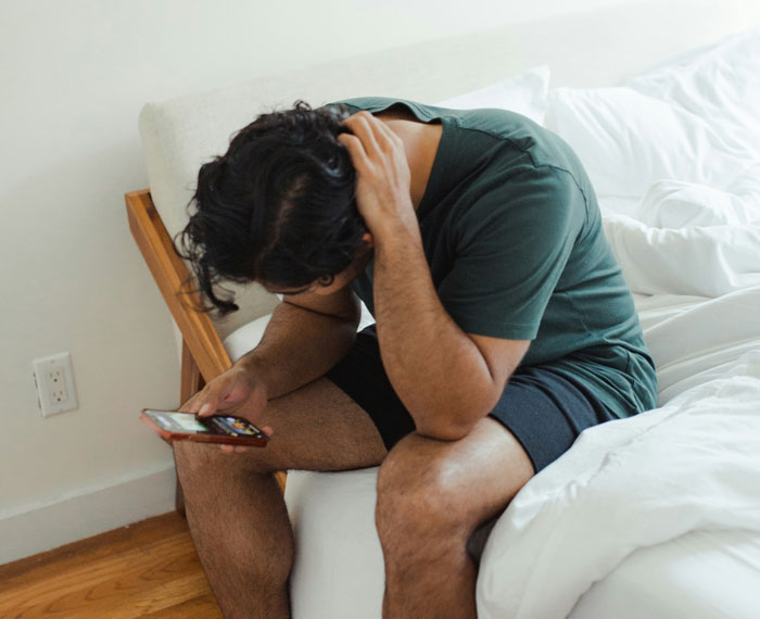 Person looking at a phone while sitting on a bed, possibly thinking about being fired.