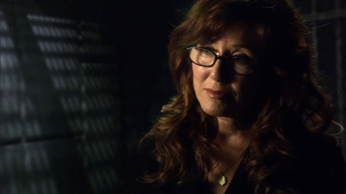 Woman with glasses in a dimly lit room, representing a strong female protagonist theme.