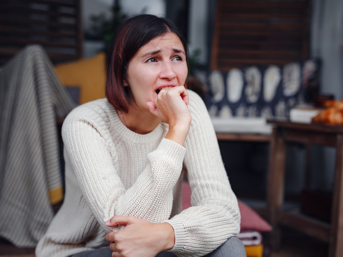 A woman looking upset in a cozy, indoor setting, wearing a white sweater, with home decor in the background.