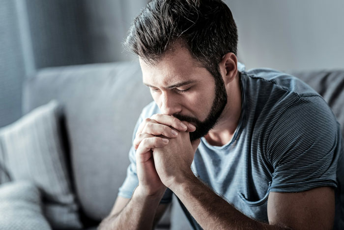 A worried husband sits on a couch, deep in thought.