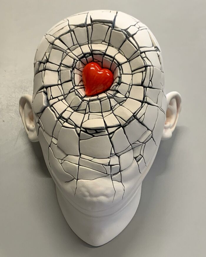 Sculpture blending realism and surrealism: a cracked head with a red heart at the center.