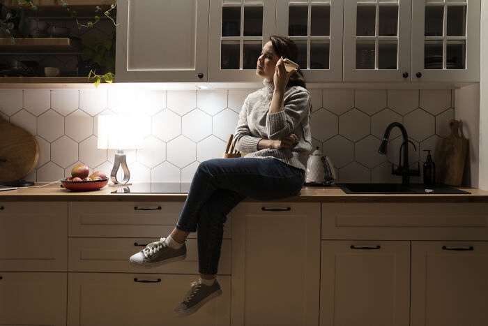 Woman sitting on a kitchen counter, demonstrating a frugal home hack in a cozy kitchen setting.