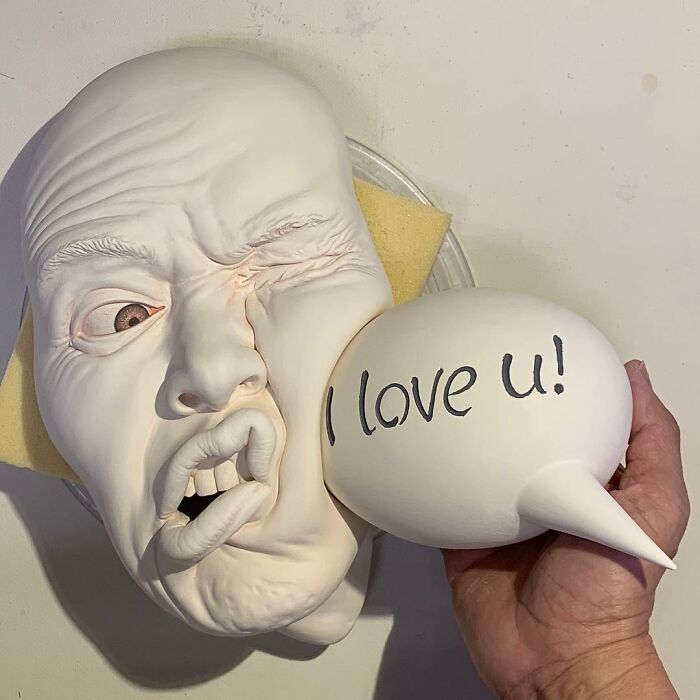 Realism and surrealism blend in expressive sculpted face with speech bubble saying “I love u!”