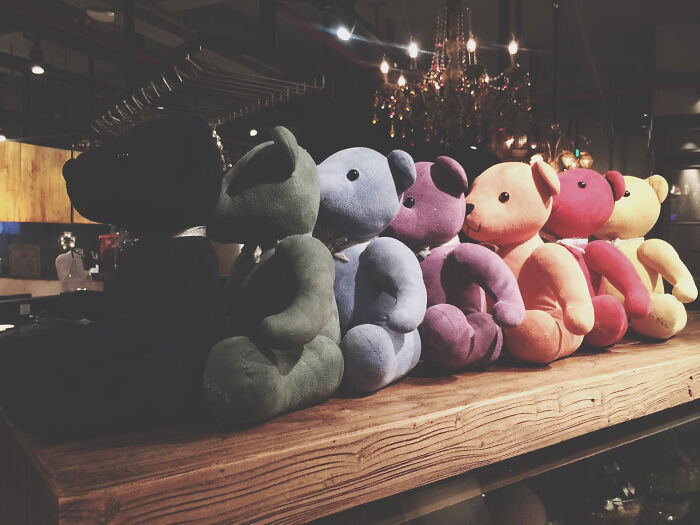 Colorful teddy bears on display, illuminated by chandeliers in a cozy setting.