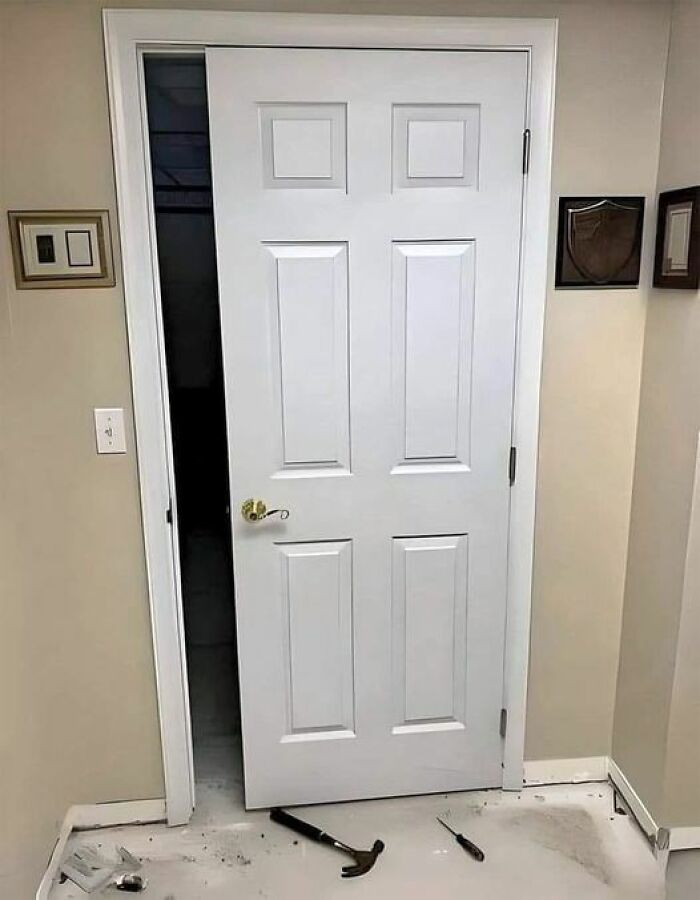 A white door installed upside down, showcasing cheap construction fails with tools on the floor.