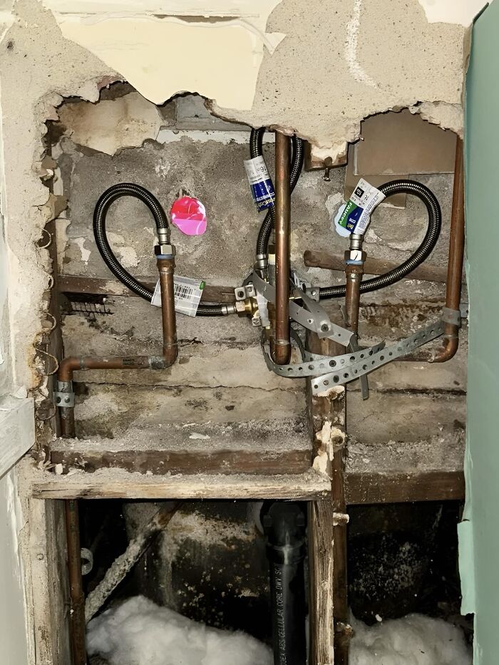 Funny cheap construction fail with tangled pipes in a messy wall opening.