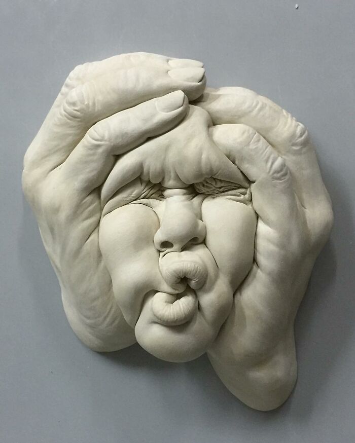 A surreal sculpture blending realism, depicting a face being squeezed by hands, showcasing expressive art techniques.