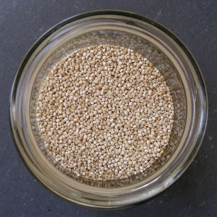 Jar of uncooked quinoa seeds viewed from above on a dark surface.