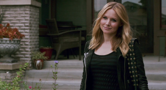 A woman with long blonde hair, wearing a studded jacket, stands confidently on a porch, embodying strong female protagonist.