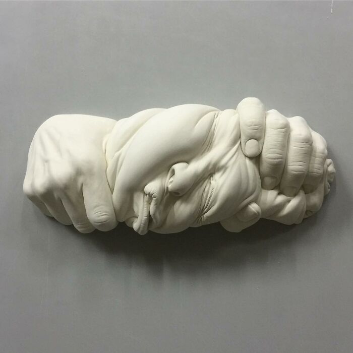 Surrealism and realism blend in a sculptor's expressive artwork depicting hands intertwined with a face.