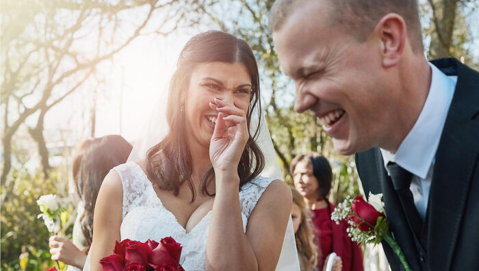 Bride and groom laughing during a wedding mishap, surrounded by guests holding flowers.