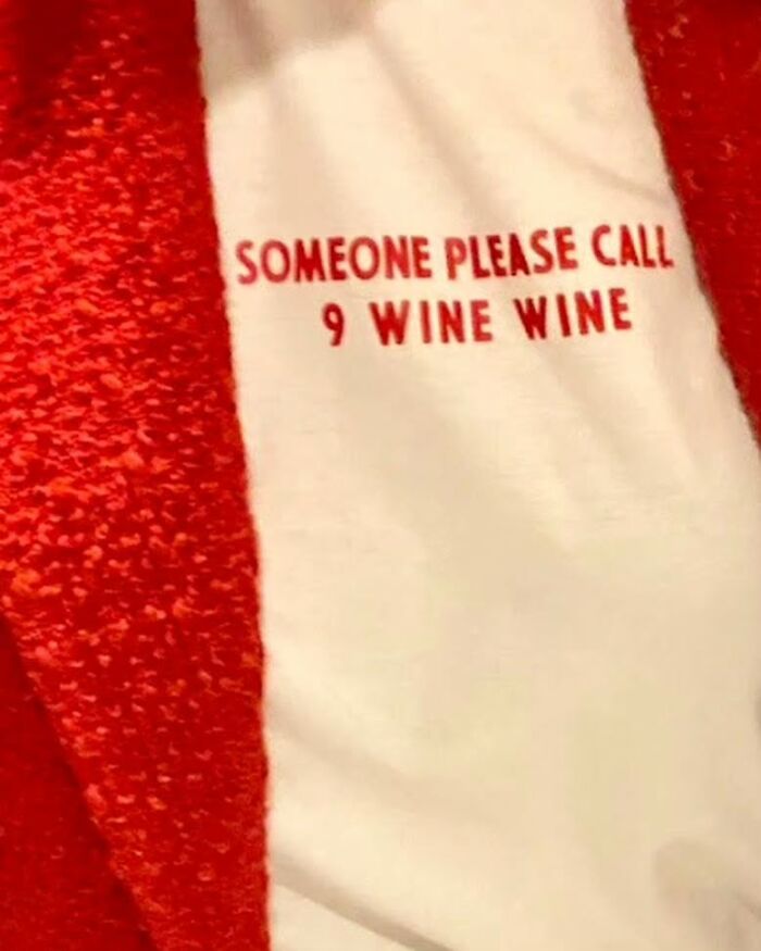 Weird shirt with red text "SOMEONE PLEASE CALL 9 WINE WINE" on white fabric.