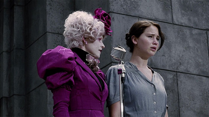 Two women stand together; one wears a bold purple outfit, embodying a strong female protagonist.