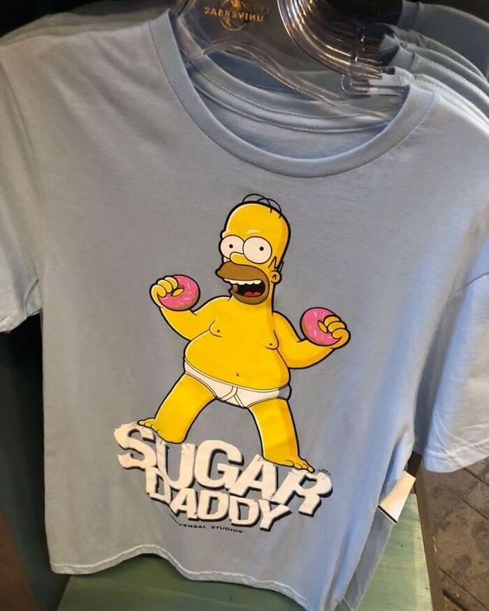 Weird-shirt with Homer Simpson holding donuts, labeled "Sugar Daddy," hanging on a rack.