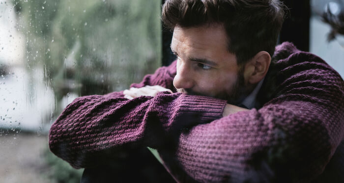 A person in a sweater looking out a rainy window, reflecting on a terrible Christmas experience.