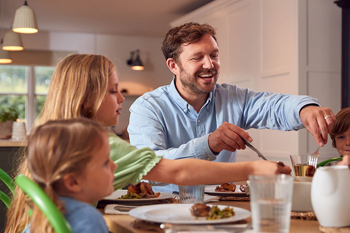 A family enjoying a meal together at home, featuring a man in a blue shirt with children at the table.