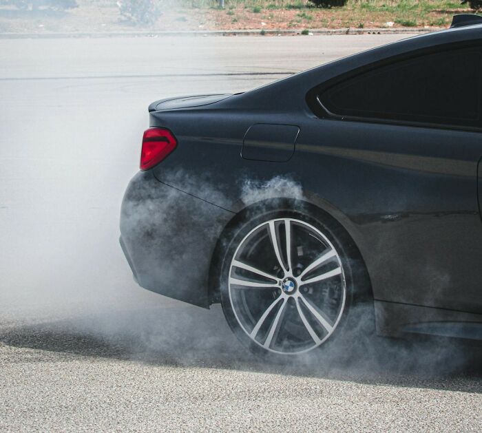 BMW car doing a burnout on asphalt, emitting smoke from the rear tire, captured from the side.