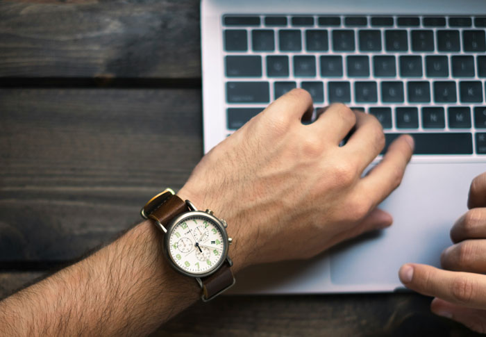 Person using a laptop with a wooden desk background, wristwatch visible, related to reasons for being fired.