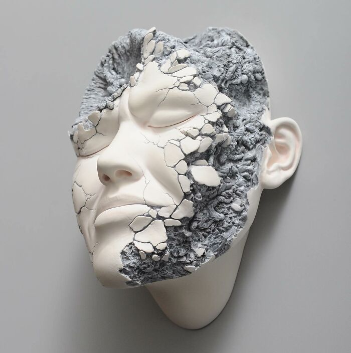 Sculpture blending realism and surrealism with a cracked, expressive face design on a smooth background.