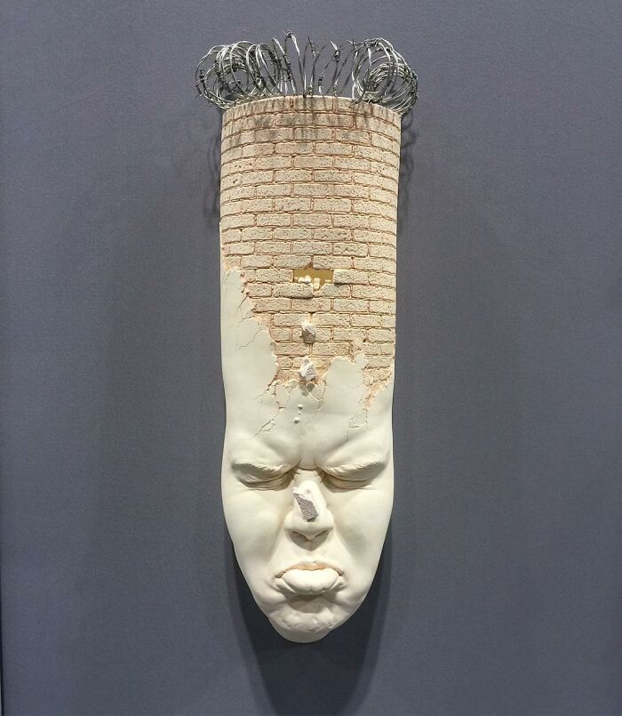 Surrealism and realism merge in a sculpted face with a cracked brick texture and wire details on top.