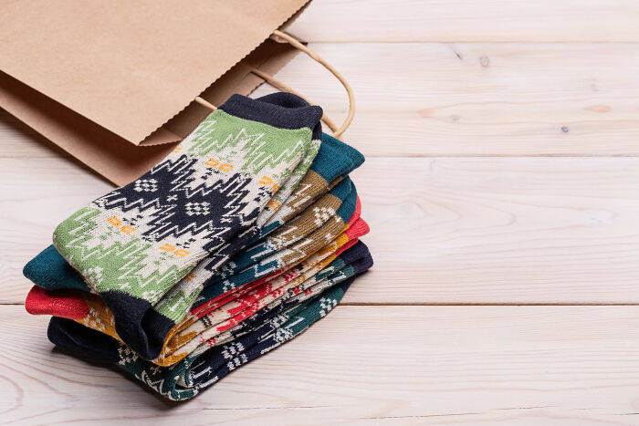 Colorful patterned socks stacked on a wooden table next to a brown paper bag.