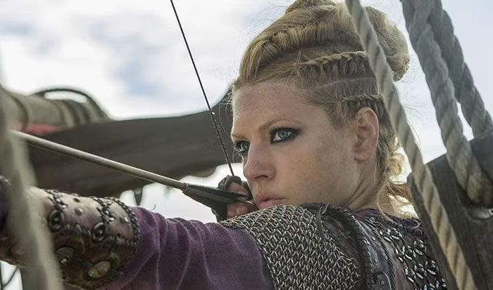 A focused female archer in medieval attire on a ship, embodying a strong female protagonist.