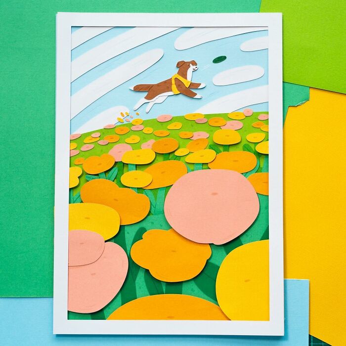 Layered paper art depicting a cute dog leaping through a vibrant field of colorful flowers under a blue sky.