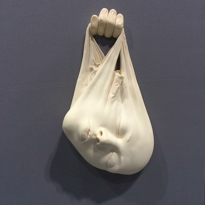 Sculpture blending realism and surrealism, featuring a face and hand emerging from stretched fabric.