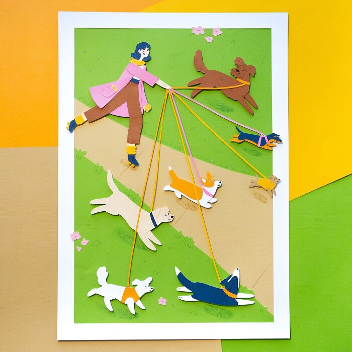 Layered paper illustration of a person walking six playful dogs on a sunny day.