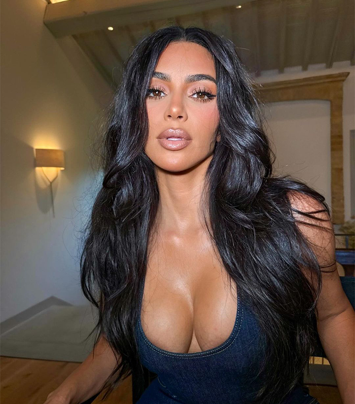 Kim Kardashian in a denim top with long hair and neutral makeup in a well-lit room.