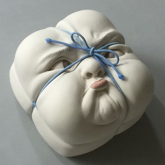 Surreal sculpture of a face in expressive art style, tied with a blue string.