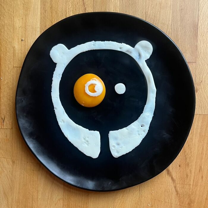 Creative fried eggs arranged like a panda on a black plate, showcasing artistic cooking techniques.