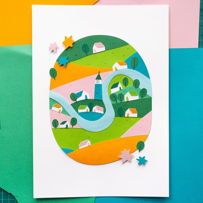 Layered paper illustration of a colorful village scene with houses, a river, and trees.