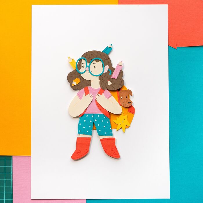 Layered paper art depicting a cute girl with glasses, colorful outfit, and a playful dog in the background.