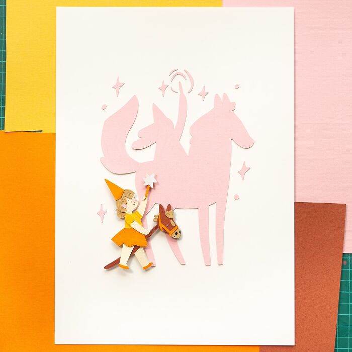 Layered paper art illustration of a girl in an orange hat and dress, holding a horse toy, with a magical pink silhouette background.