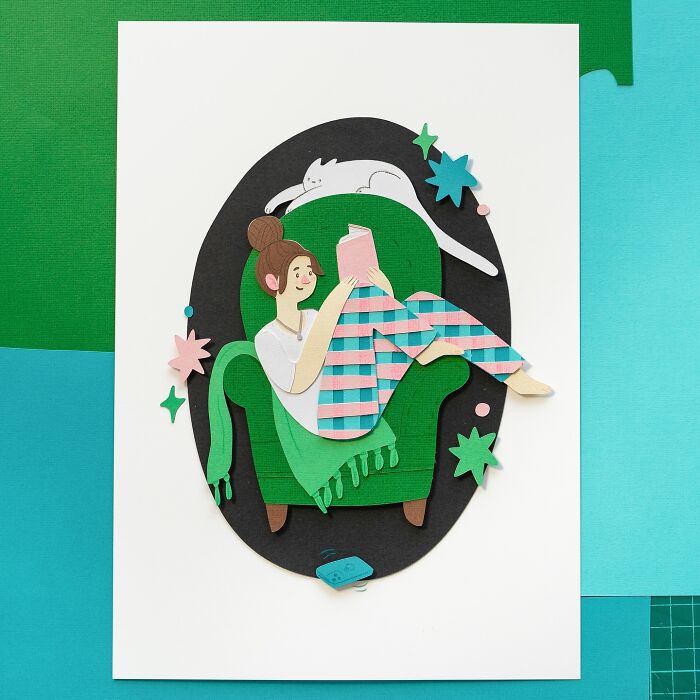 Layered paper illustration of a woman reading on a green chair with a cat and stars.