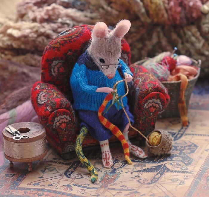 Miniature mouse in a blue sweater knitting on a patterned armchair, part of Maggie Rudy's detailed Mouseland world.