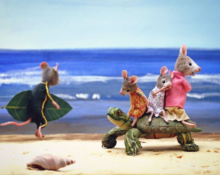 Miniature mice in colorful outfits riding a turtle on the beach in Mouseland.