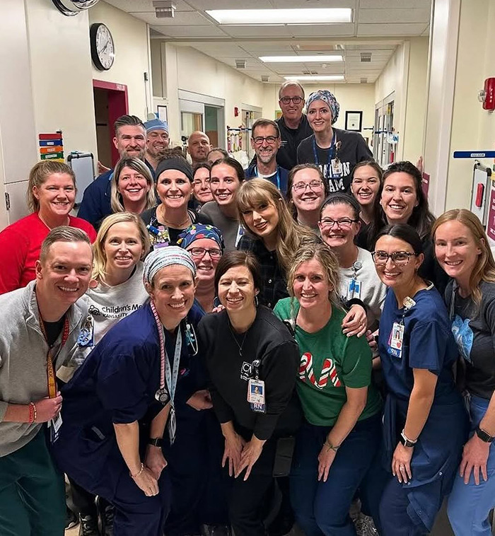 Taylor Swift visiting a children\'s hospital, pictured with a group of smiling healthcare staff and team members.