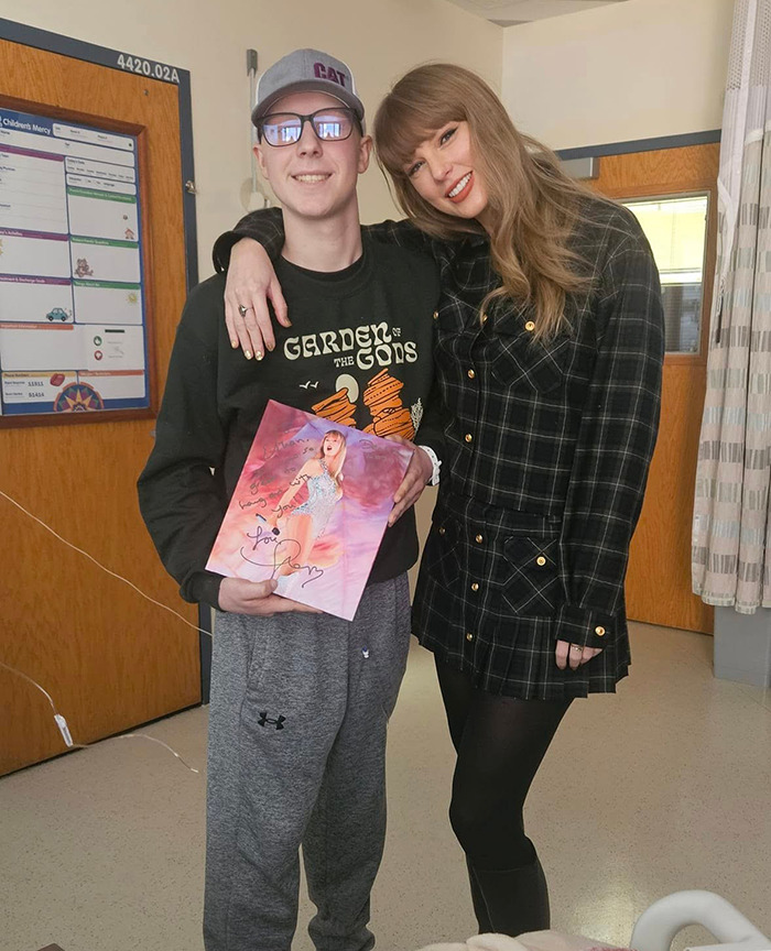 Taylor Swift visits a children\'s hospital, smiling with a fan holding her album.