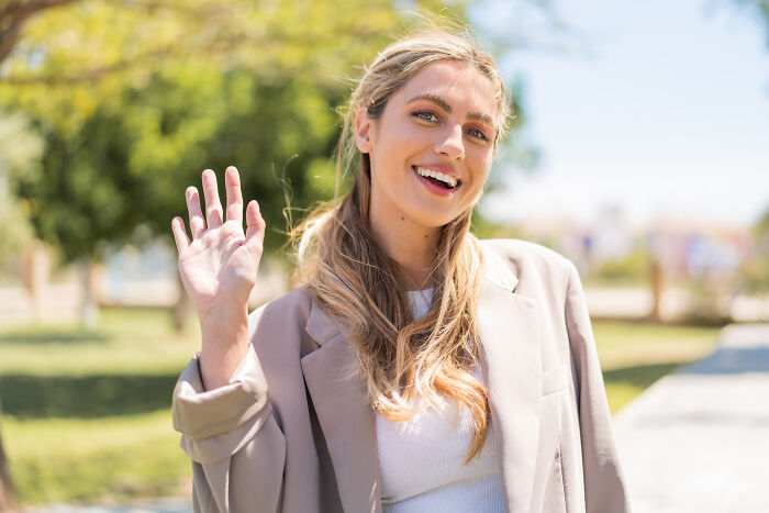 Person smiling and waving in a park, embodying a cringeworthy travel moment.