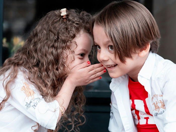 Two kids whisper and giggle, dressed casually, symbolizing carefree vacation vibes.